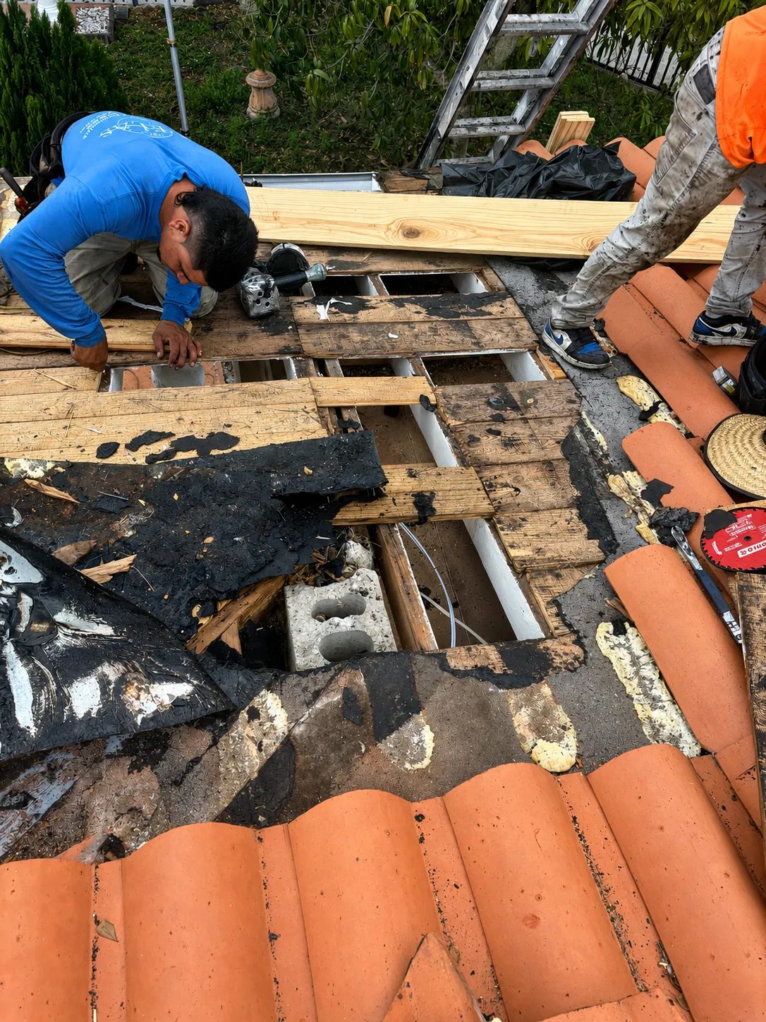 Skymen Roofing crew replacing rotted roof decking under a clay tile roof